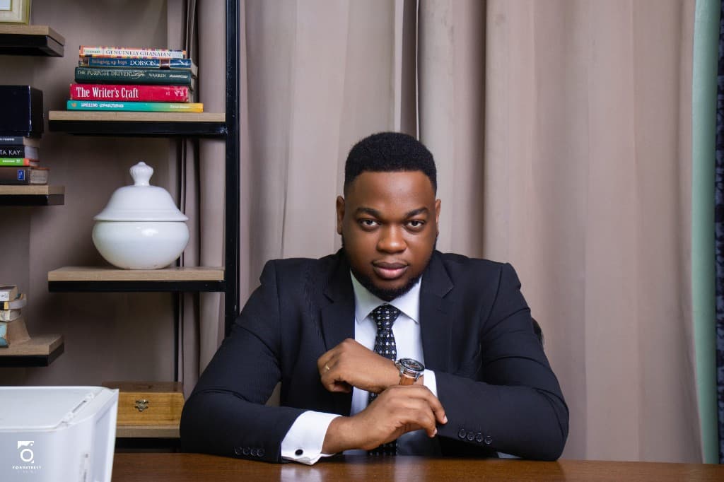 Samuel Adanuvo seated at a desk in a dark suit